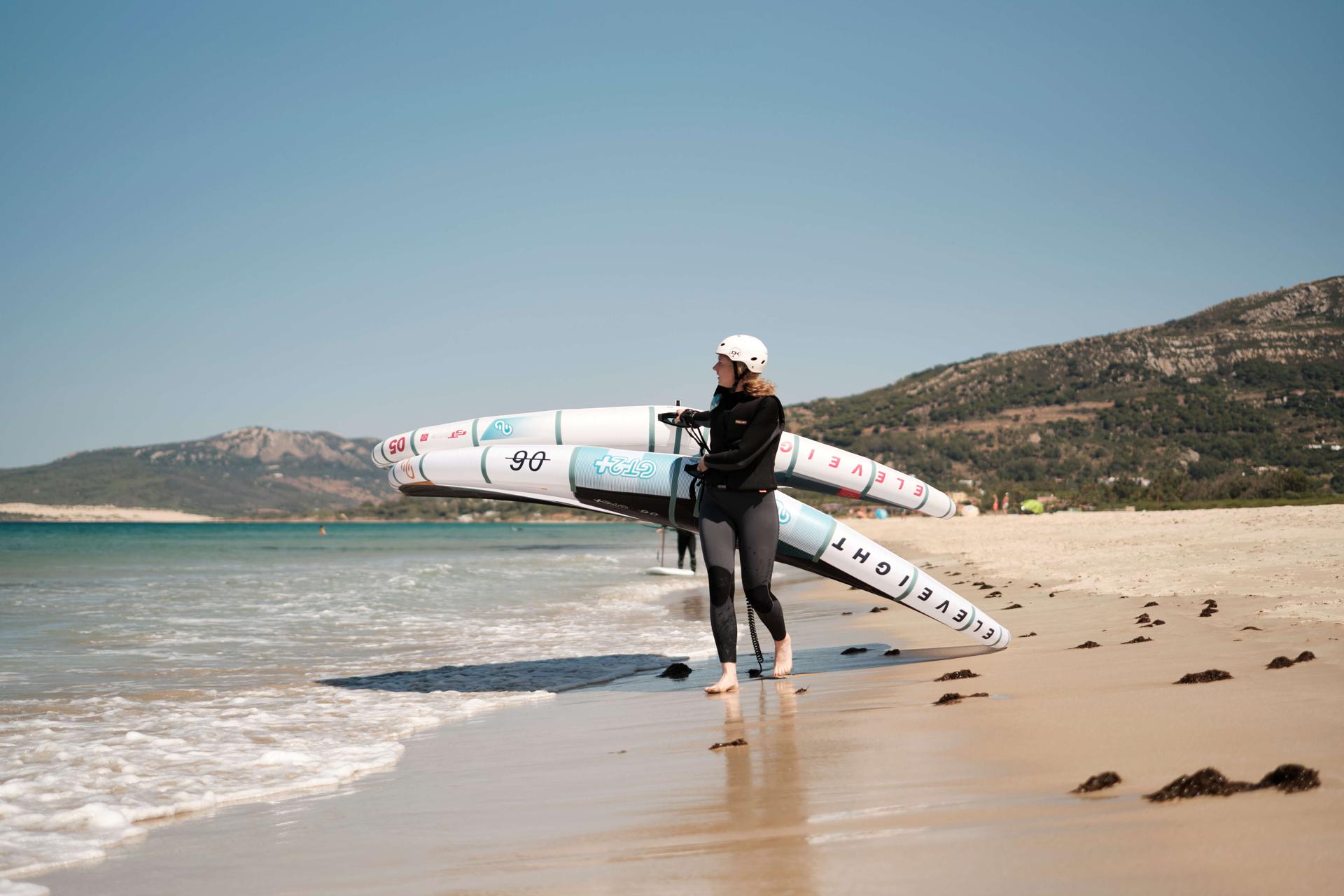 Student carrying two wing foil sails on the beach.